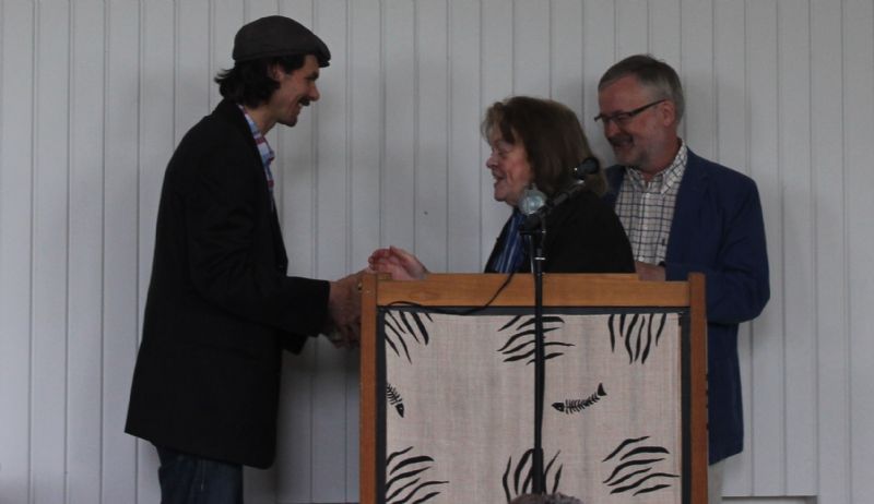 Michel Wenzer tar emot ett halvt dussin böcker som Jan Fridegård skrivit och ett hedersmedlemskap i sällskapet av Aase Fridegård och Mats O Karlsson den 13 juni 2014.